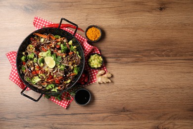 Photo of Stir-fry. Tasty noodles with meat in wok and ingredients on wooden table, flat lay. Space for text