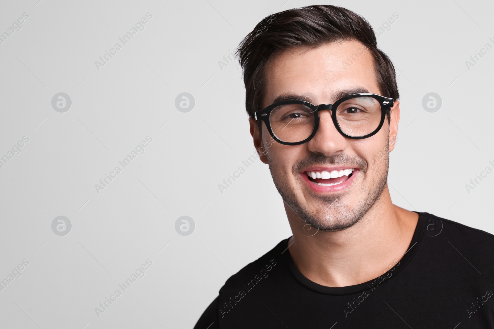 Photo of Portrait of handsome young man in black t-shirt with glasses on grey background. Space for text