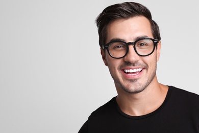 Photo of Portrait of handsome young man in black t-shirt with glasses on grey background. Space for text