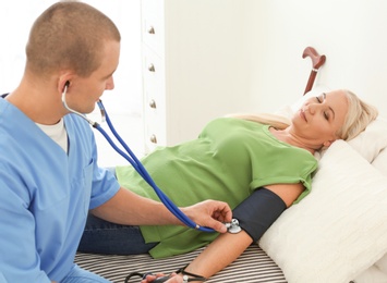 Photo of Male medical assistant measuring female patient blood pressure during home visit