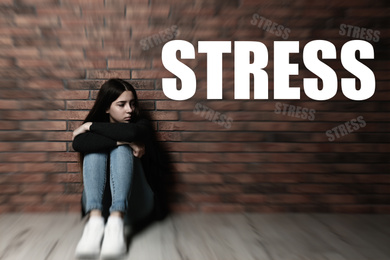 Image of Word STRESS and depressed young girl sitting on floor near brick wall 