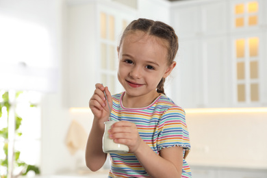 Photo of Cute little girl with tasty yogurt in kitchen