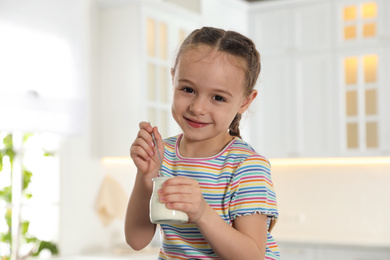 Cute little girl with tasty yogurt in kitchen