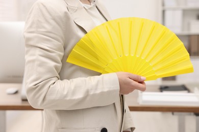 Businesswoman with yellow hand fan in office, closeup
