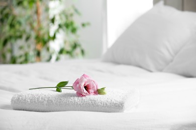 Photo of White towel with beautiful flower on bed indoors, space for text