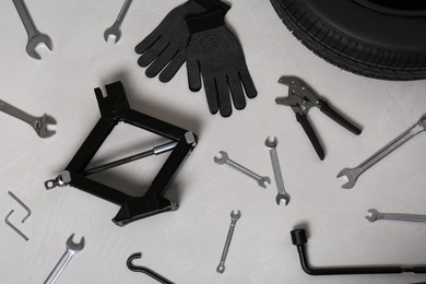 Photo of Car wheel, scissor jack, gloves and different tools on grey surface, flat lay