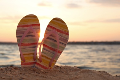 Stylish flip flops on sand near sea, space for text. Beach accessories