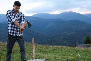 Photo of Handsome man with axe cutting firewood in mountains