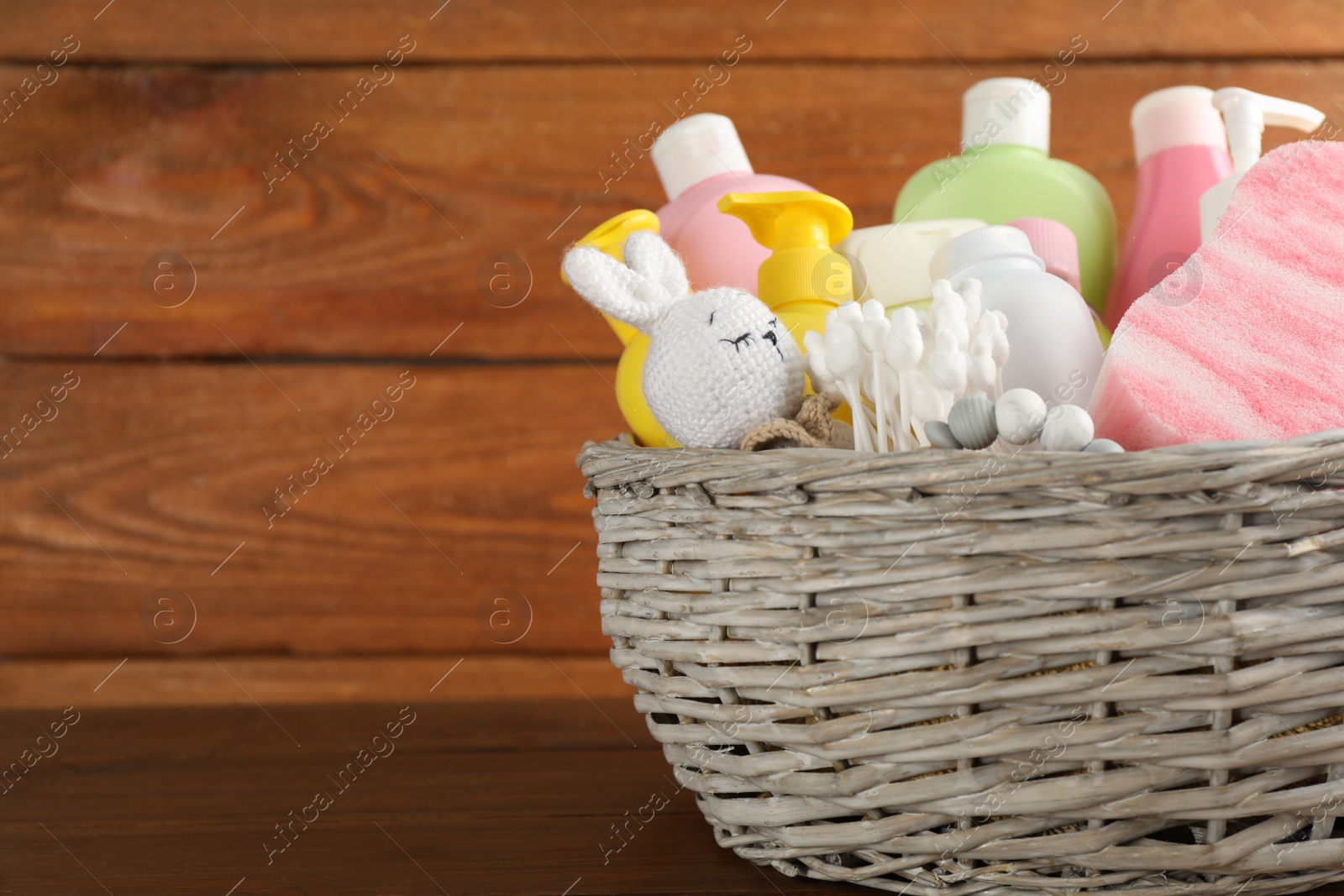Photo of Wicker basket full of different baby cosmetic products, accessories and toys on wooden table. Space for text