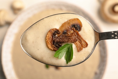 Photo of Spoon with fresh homemade mushroom soup over bowl, top view