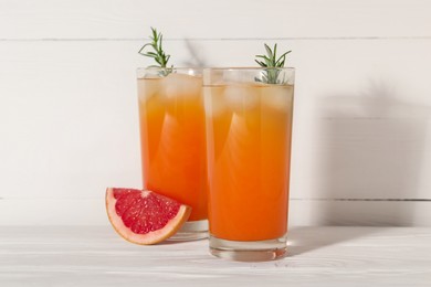 Photo of Tasty grapefruit drink with ice and rosemary in glasses on white wooden table