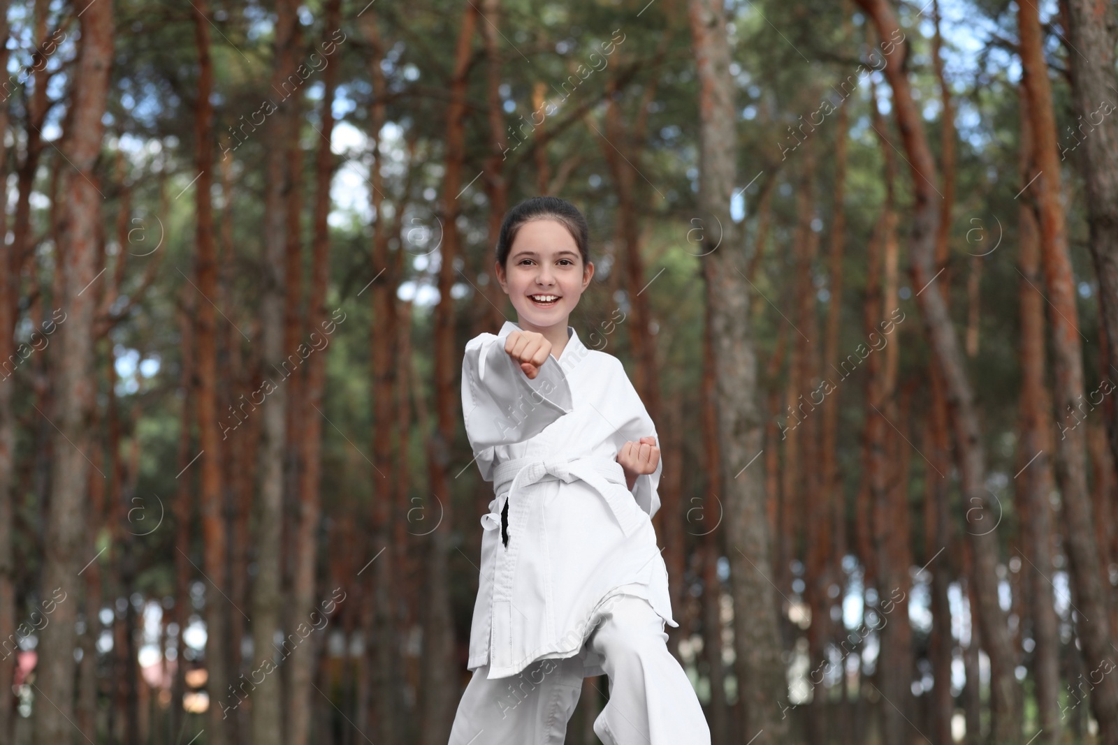 Photo of Cute little girl in kimono practicing karate in forest