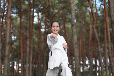 Photo of Cute little girl in kimono practicing karate in forest