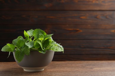 Photo of Fresh lemon balm in bowl on wooden table, space for text