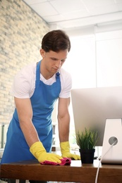 Photo of Young man in apron and gloves cleaning office