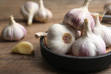 Fresh organic garlic in bowl on wooden table, closeup