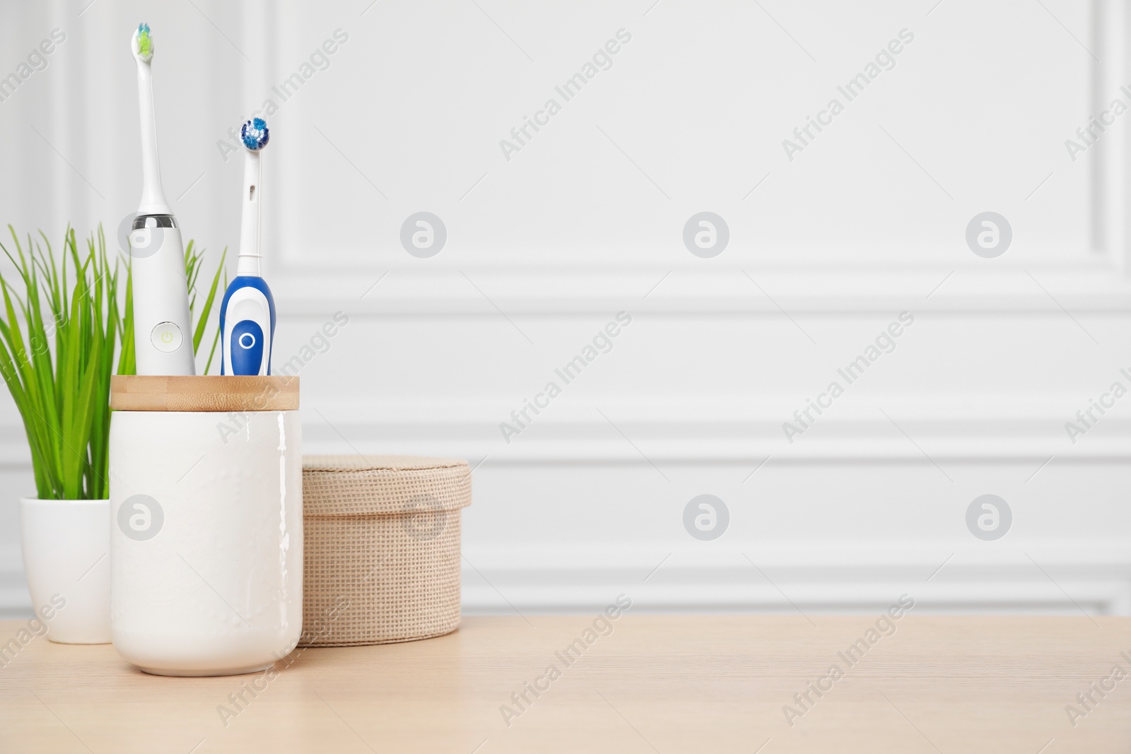 Photo of Electric toothbrushes in holder on wooden table. Space for text