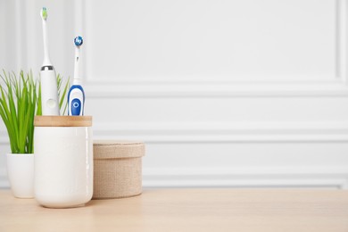 Photo of Electric toothbrushes in holder on wooden table. Space for text