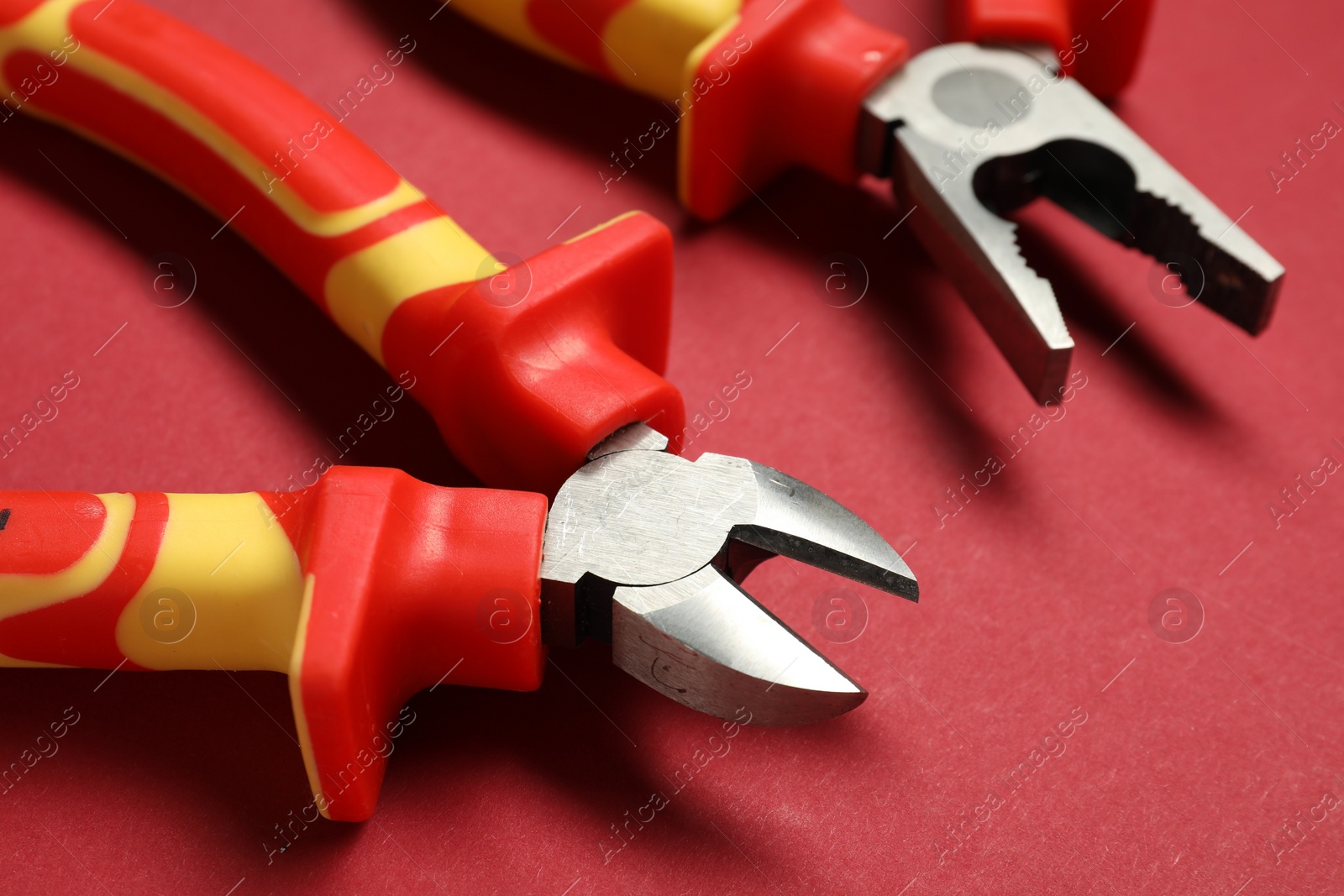 Photo of Two pliers on red background, closeup view