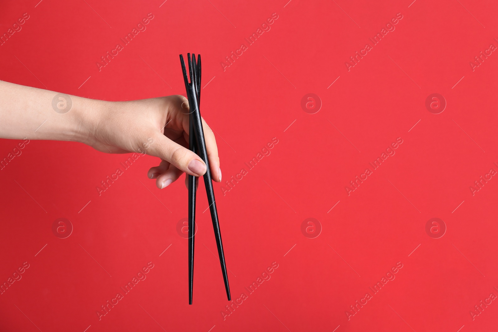 Photo of Woman holding pair of black chopsticks on red background, closeup. Space for text