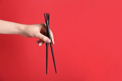 Woman holding pair of black chopsticks on red background, closeup. Space for text