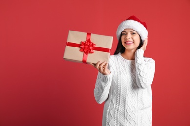 Photo of Young beautiful woman in Santa hat with gift box on color background. Christmas celebration