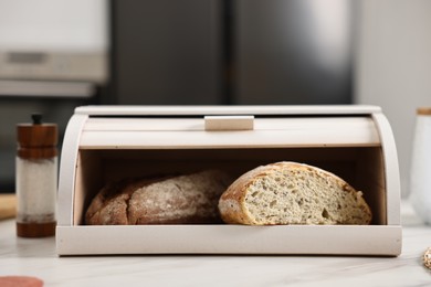 Photo of Wooden bread basket with freshly baked loaves on white marble table in kitchen