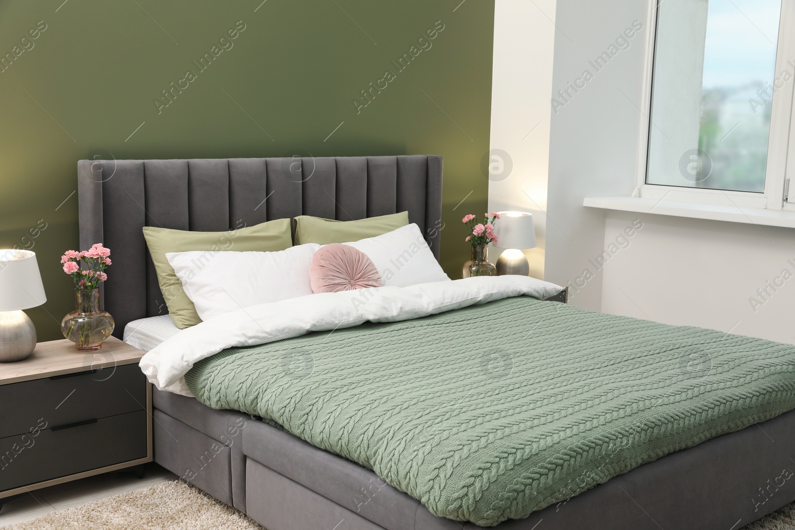 Photo of Large comfortable bed, lamps and beautiful flowers in stylish room. Interior design
