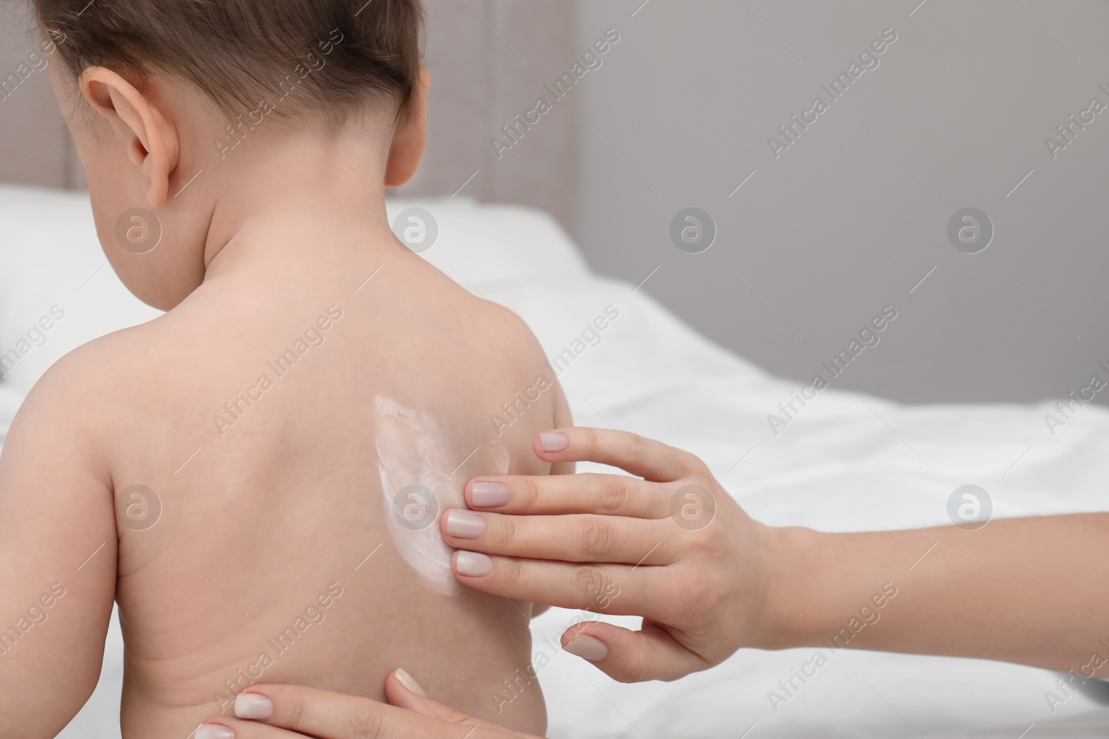 Photo of Mother applying body cream on her baby indoors, closeup