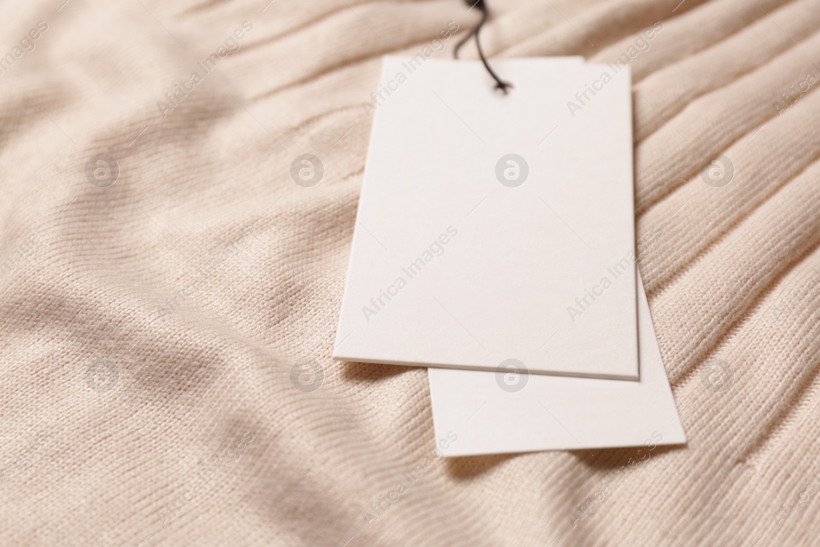 Photo of Blank white tags on beige sweater, closeup. Space for text