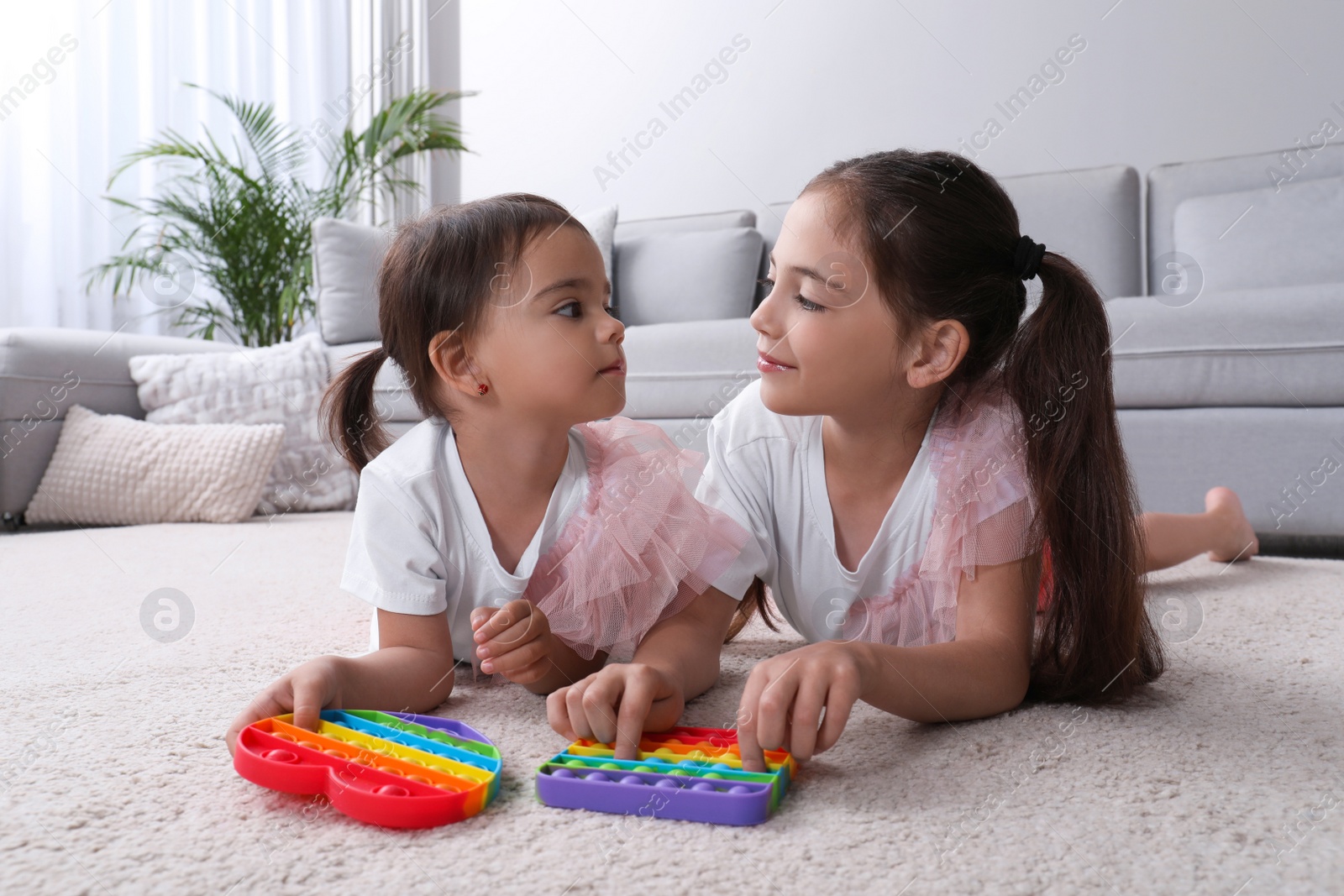 Photo of Little girls playing with pop it fidget toys on floor at home