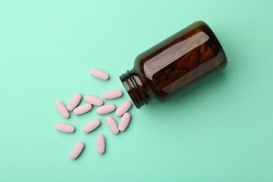 Photo of Vitamin pills and bottle on mint color background, top view