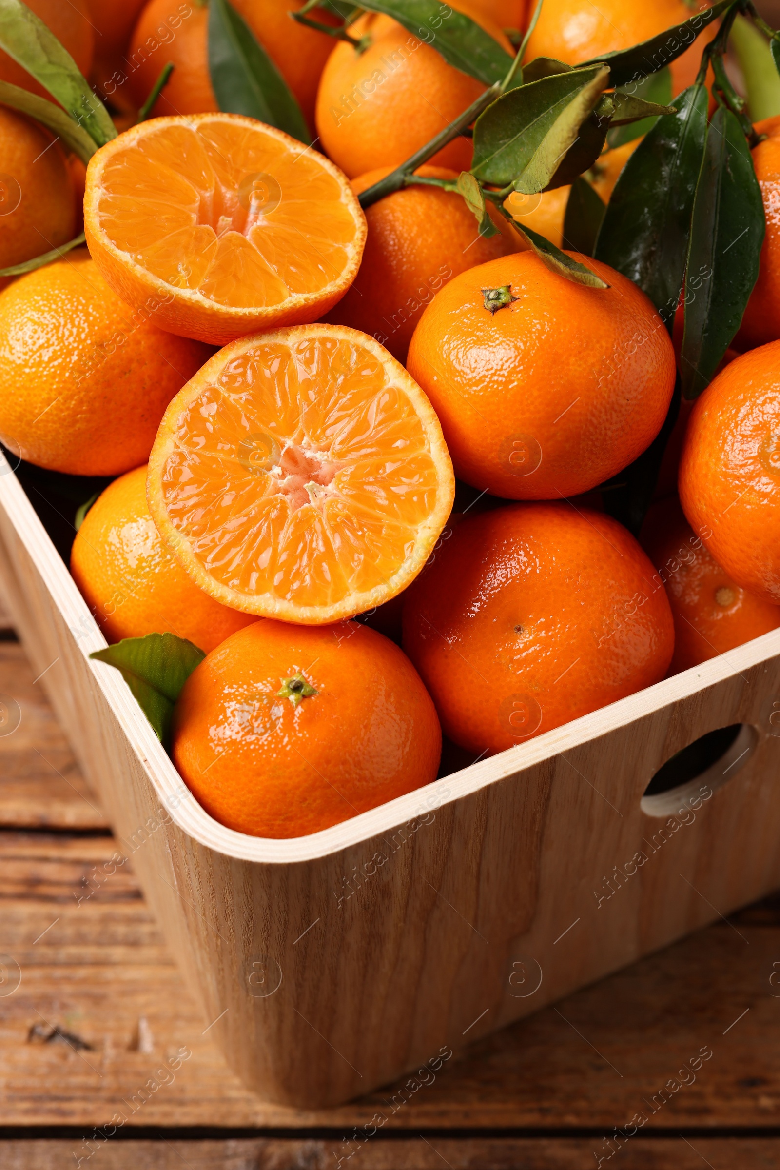 Photo of Fresh tangerines with green leaves in crate on wooden table, closeup