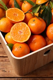 Fresh tangerines with green leaves in crate on wooden table, closeup