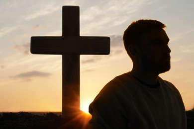 Atheism. Silhouette of man turned away from Christian cross outdoors at sunrise