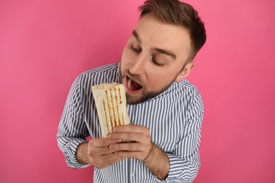 Young man eating delicious shawarma on pink background