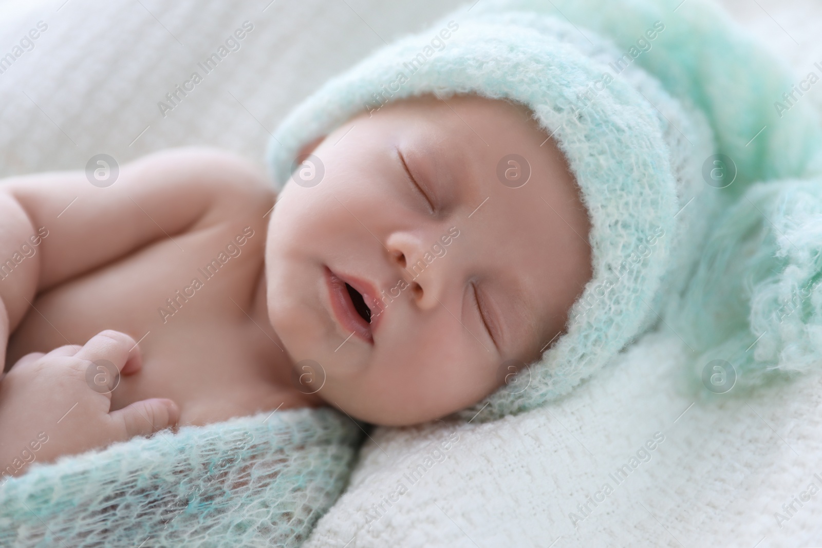 Photo of Cute newborn baby in warm hat sleeping on white plaid, closeup