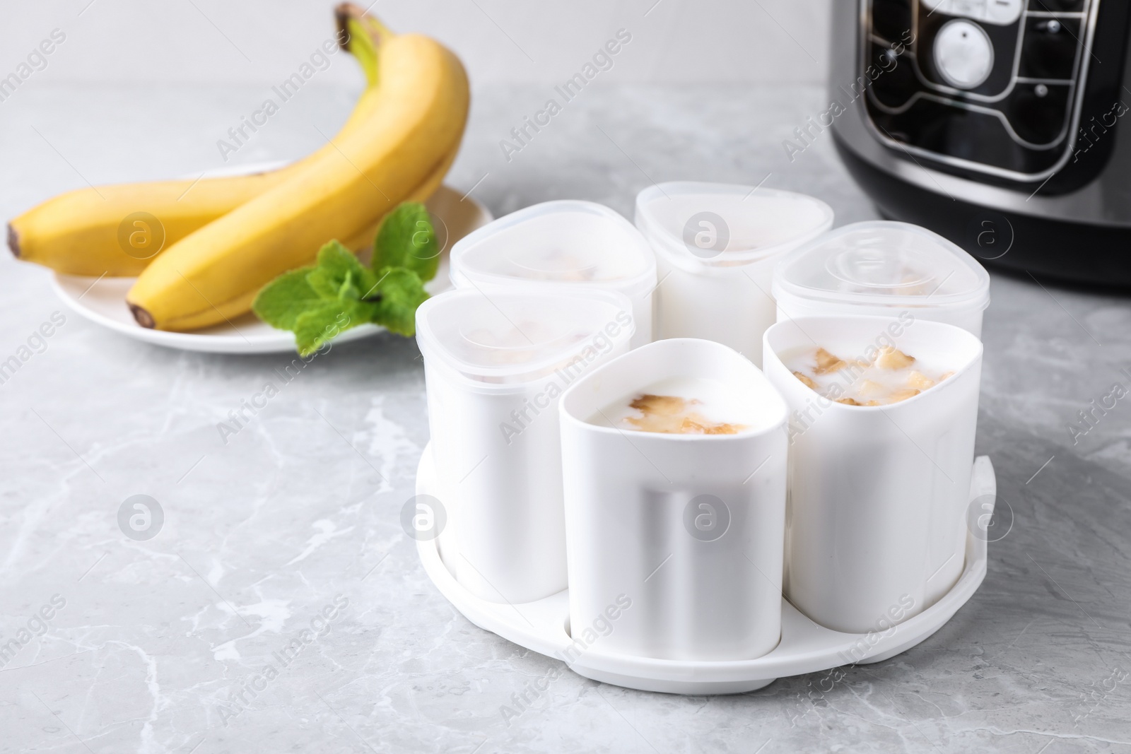 Photo of Cups of yogurt with bananas and multi cooker on table