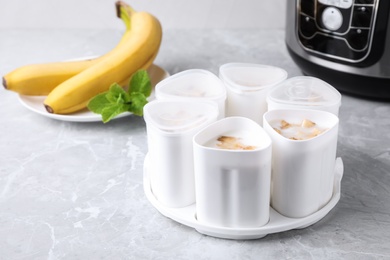 Photo of Cups of yogurt with bananas and multi cooker on table