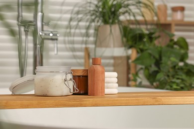 Photo of Wooden board with spa products on bath tub in bathroom, space for text