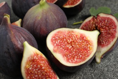 Photo of Whole and cut ripe figs on grey textured table, closeup