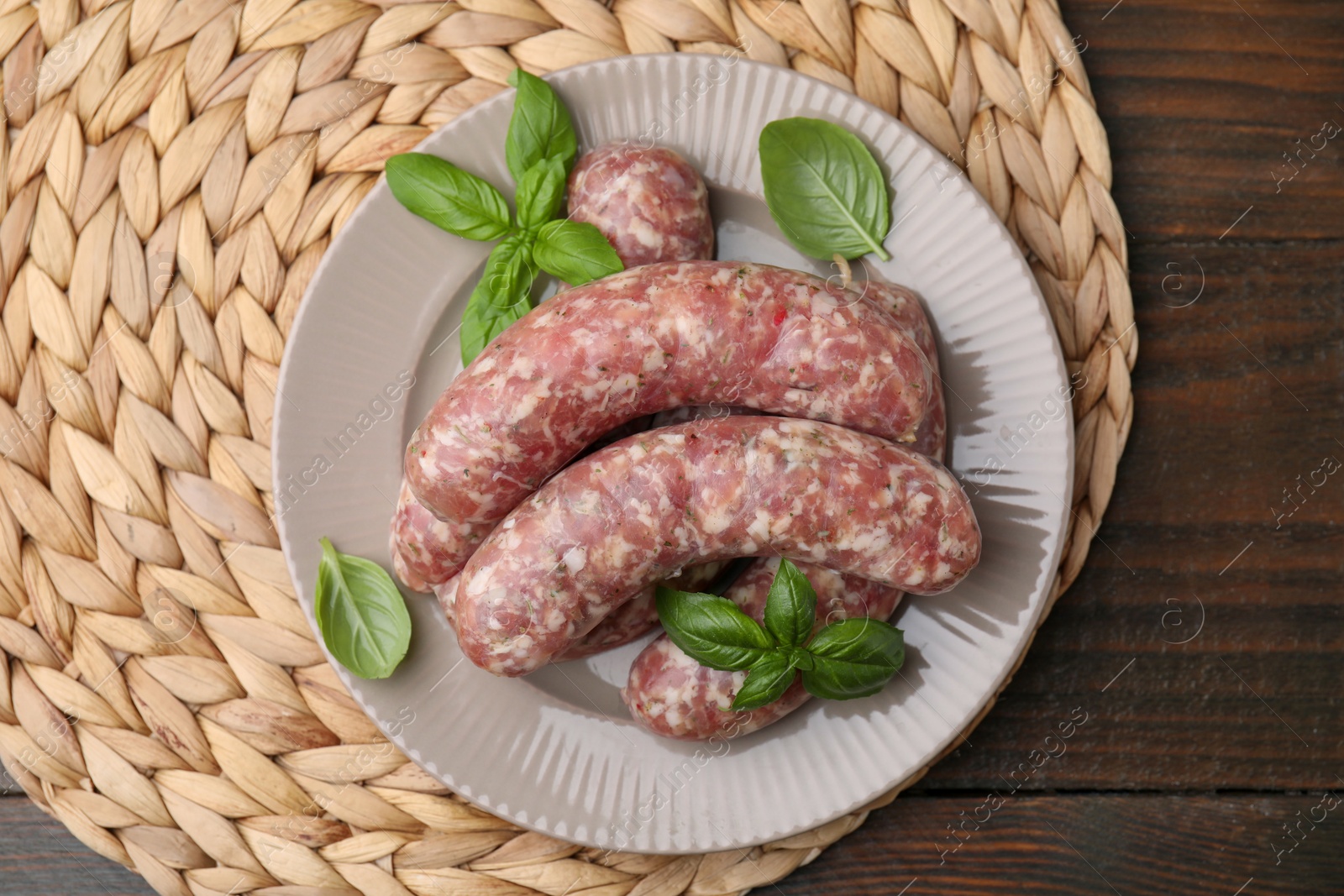 Photo of Raw homemade sausages and basil leaves on wooden table, top view