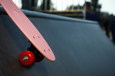 Photo of Modern pink skateboard with red wheels on ramp outdoors, closeup. Space for text