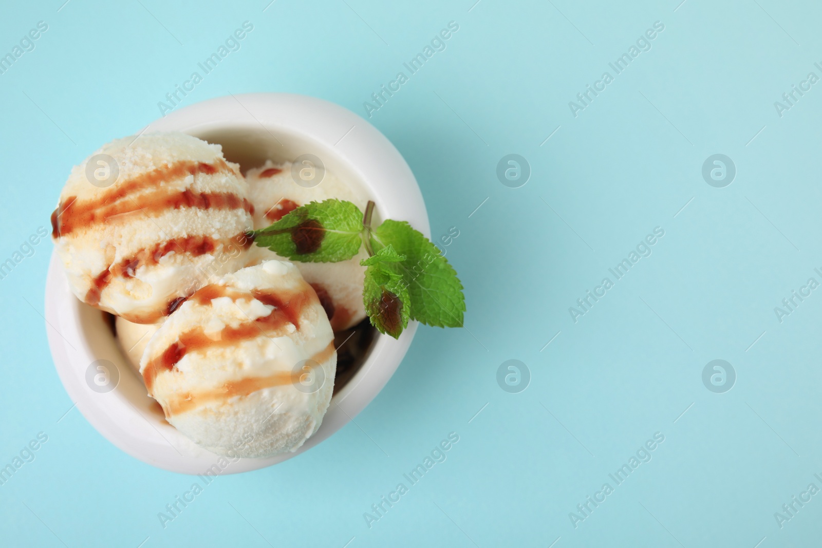 Photo of Scoops of tasty ice cream with mint leaves and caramel sauce on light blue background, top view. Space for text
