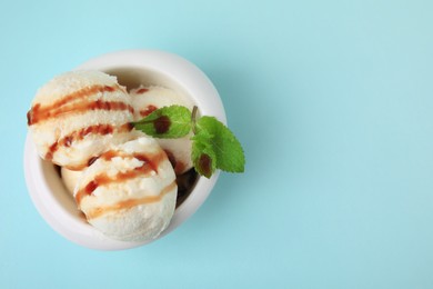 Photo of Scoops of tasty ice cream with mint leaves and caramel sauce on light blue background, top view. Space for text