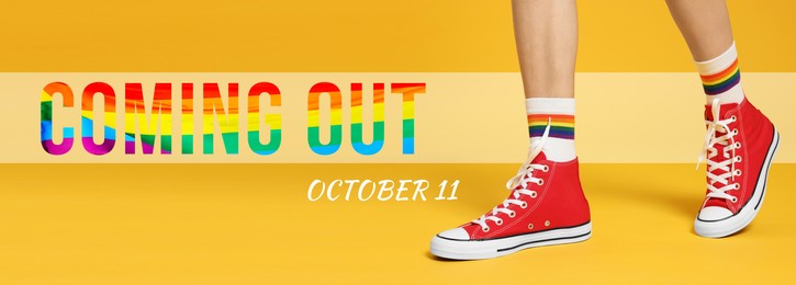 Image of National Coming Out day, October 11. Woman in gumshoes and socks with pride rainbow on yellow background, closeup. Banner design