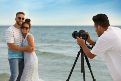 Photographer taking picture of couple with professional camera near sea