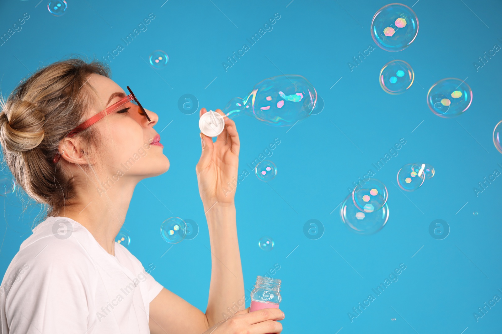 Photo of Young woman blowing soap bubbles on light blue background, space for text