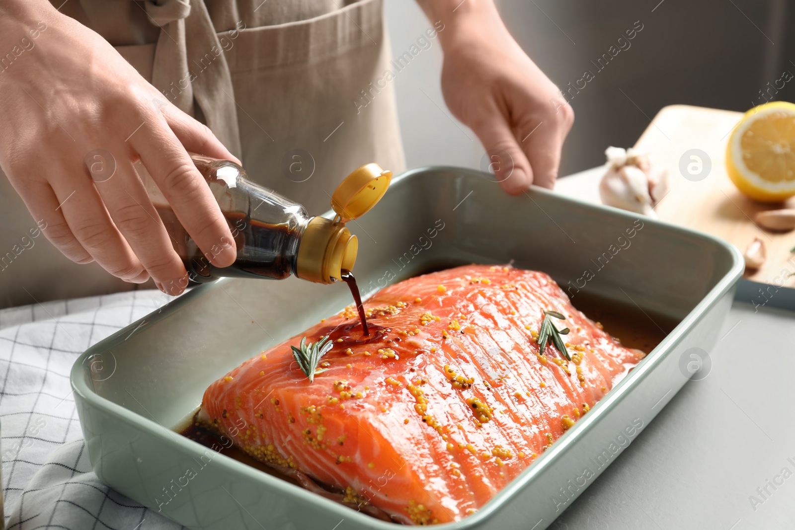 Photo of Woman pouring marinade onto raw salmon in baking dish, closeup