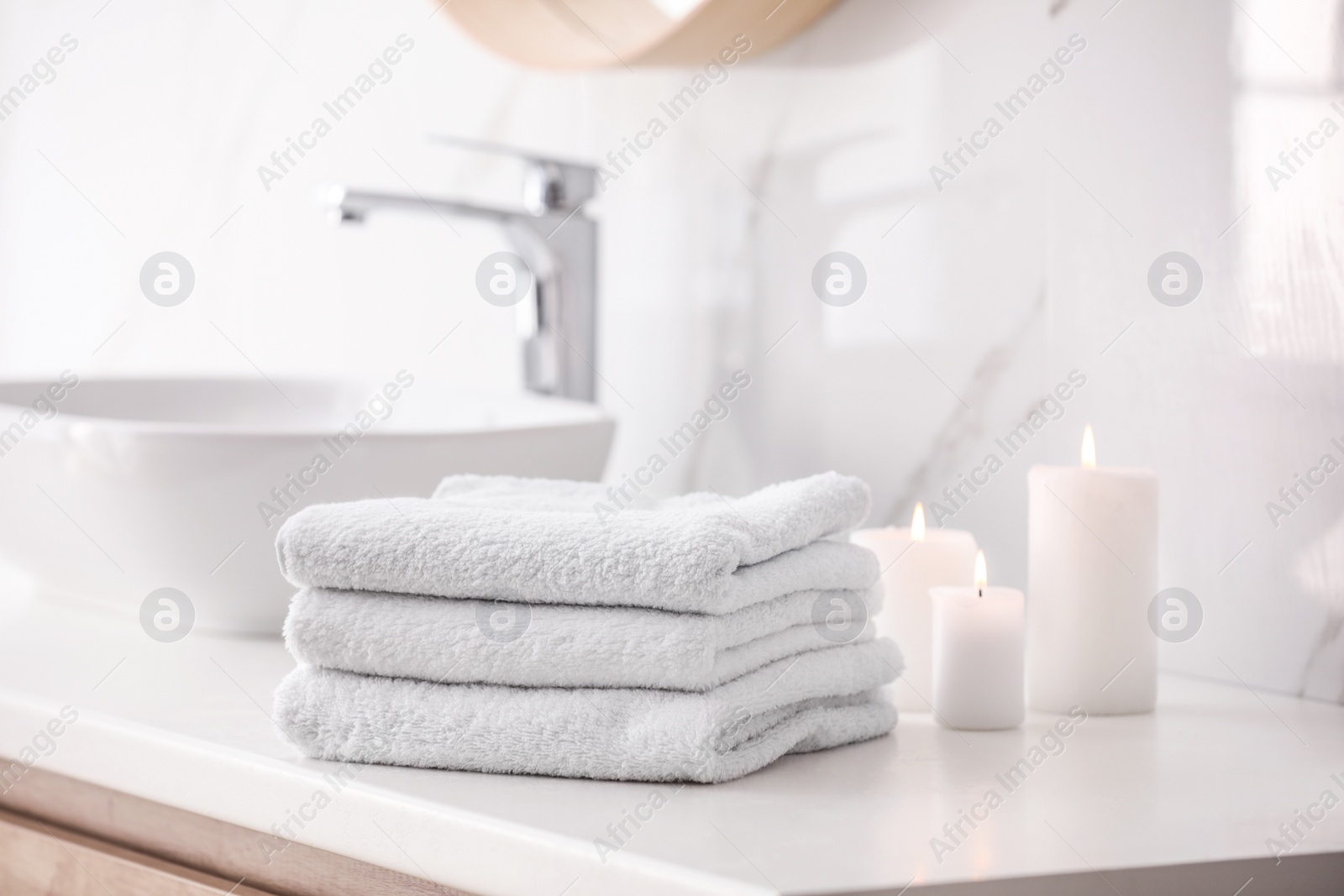 Photo of Stack of fresh towels and burning candles on countertop in bathroom